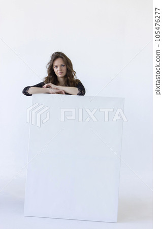 Young Real Woman Stands Behind White Blank Large Stretched Canvases for Painting. Beautiful Artist Poses With Empty Boards On White Background Indoor. Mockup. Horizontal Plane. Copy Space 105476277