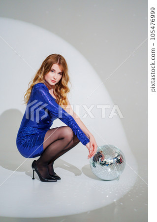 woman in shiny blue dress on floor with a disco ball on a white room 105476999