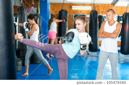 Young woman performing punching bag heel kick during workout in gym 105479380