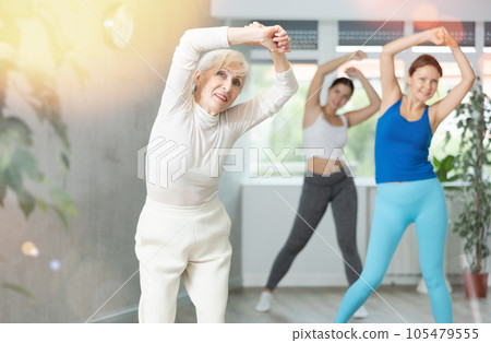Cheerful senior woman training zumba with group Cheerful senior woman training zumba with group 105479555