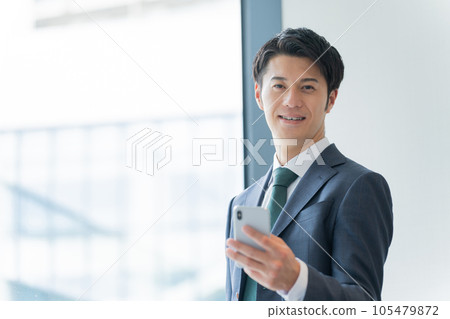 A businessman who uses a smartphone in the office A businessman who uses a smartphone in the office 105479872