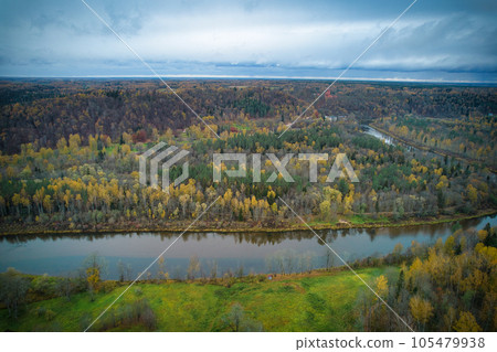 Above aerial shot of green pine forests and yellow foliage groves with beautiful texture of golden treetops. Beautiful fall season scenery in evening. Mountains in autumn colors in golden time Above aerial shot of green pine forests and yellow foliage groves with beautiful texture of golden treetops. Beautiful fall season scenery in evening. Mountains in autumn colors in golden time 105479938