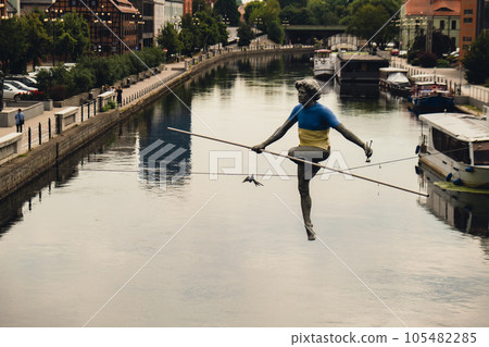 Bydgoszcz, Poland - August 2022 Brda river in Bydgoszcz Man crossing a river sculpture , of a man balancing on a wire, old granary building, Kuyavian-Pomerania. Old town with reflection in Brda River 105482285