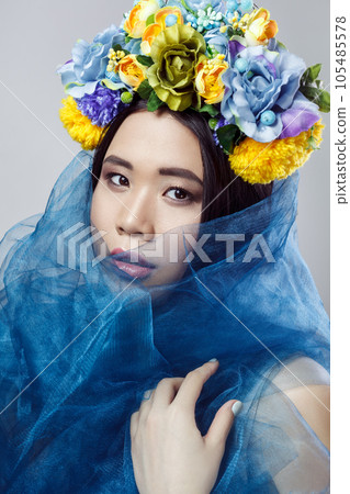 Closeup portrait of sensual beautiful woman with makeup and with floral hat and blue veil, looking at camera with serious expression. Indoor studio shot isolated on gray background Closeup portrait of sensual beautiful woman with makeup and with floral hat and blue veil, looking at camera with serious expression. Indoor studio shot isolated on gray background 105485578