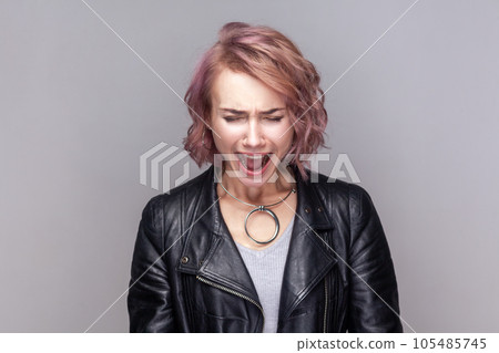 Portrait of despair sad depressed woman with short hairstyle standing screaming loud, having problems on her work, wearing black leather jacket. Indoor studio shot isolated on grey background. 105485745