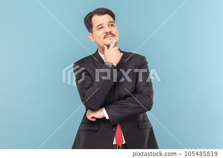 Portrait of confused pensive puzzled man with mustache standing holding chin, thinking about his work, wearing black suit with red tie. Indoor studio shot isolated on light blue background. Portrait of confused pensive puzzled man with mustache standing holding chin, thinking about his work, wearing black suit with red tie. Indoor studio shot isolated on light blue background. 105485819