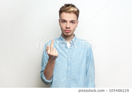 Portrait of rude serious impolite man wearing denim shirt showing middle finger, arguing with somebody, looking at camera with bossy expression. Indoor studio shot isolated on gray background. 105486229