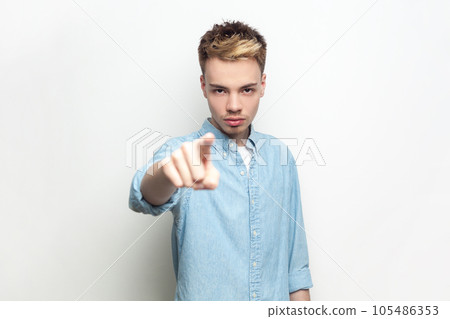 Portrait of bossy strict man wearing denim shirt looking and indicating to camera, choosing you, you have problems, has serious expression. Indoor studio shot isolated on gray background. 105486353