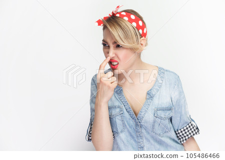 You are liar. Portrait of funny foolish blonde woman wearing blue denim shirt and red headband standing touching her nose, frowning face. Indoor studio shot isolated on gray background. You are liar. Portrait of funny foolish blonde woman wearing blue denim shirt and red headband standing touching her nose, frowning face. Indoor studio shot isolated on gray background. 105486466