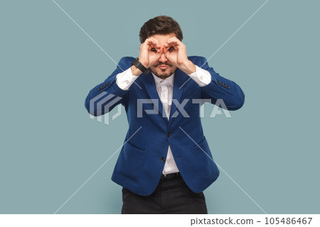 Portrait of attractive man with mustache standing with binocular gesture, looking far away, expecting good future, wearing official style suit. Indoor studio shot isolated on light blue background. 105486467