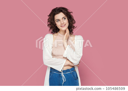 Portrait of friendly pleased smiling woman with curly hair wearing casual style outfit, looking away, dreaming about something pleasant. Indoor studio shot isolated on pink background. 105486509