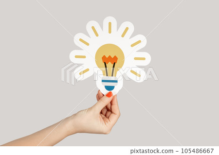 Closeup of woman hand showing paper bulb, symbol of creative idea and inspiration. Indoor studio shot isolated on gray background. 105486667