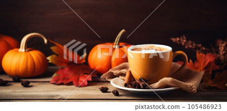 Mug of coffee and autumn leaves with orange pumpkin on wooden table. Autumn drink concept. 105486923