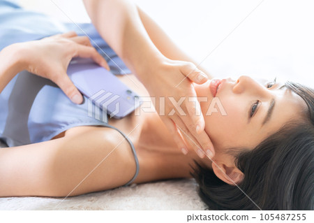 A young woman lying down and holding a smartphone and doing skin care A young woman lying down and holding a smartphone and doing skin care 105487255