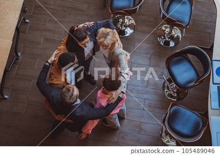 Top view of team of successful colleagues laughing and hugging while standing in circle in coworking Top view of team of successful colleagues laughing and hugging while standing in circle in coworking 105489046