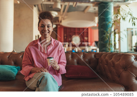 Female freelancer enjoying rest break in co-working space while drink coffee and looking at camera Female freelancer enjoying rest break in co-working space while drink coffee and looking at camera 105489085