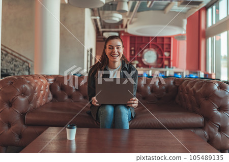 Smiling woman sales manager sitting on sofa and working on laptop on coworking background Smiling woman sales manager sitting on sofa and working on laptop on coworking background 105489135