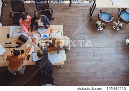 Top view of colleagues putting their arms in centre standing at modern office. Community concept 105489230