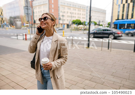Business woman talking phone whiile standing on modern building background and drinking coffee Business woman talking phone whiile standing on modern building background and drinking coffee 105490023