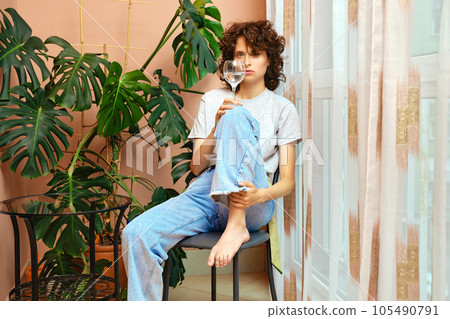 Woman with glass of water sits by the window 105490791