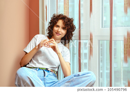 Cheerful woman sitting by window and smiling Cheerful woman sitting by window and smiling 105490796