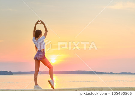 Woman raised her hands up and folded her palms in shape of heart against of sunset Woman raised her hands up and folded her palms in shape of heart against of sunset 105490806