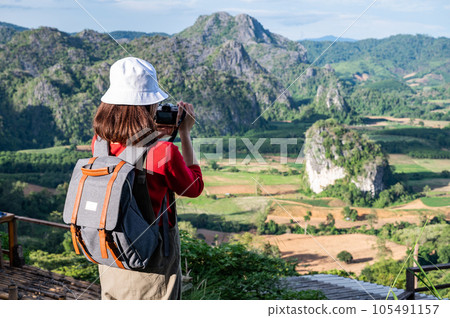 Back view of young tourist woman looking to beautiful scenery view of Pha Chang Noi in Phu Langka Forest Park during green season in Phayao province of Thailand. Back view of young tourist woman looking to beautiful scenery view of Pha Chang Noi in Phu Langka Forest Park during green season in Phayao province of Thailand. 105491157