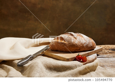 oaf of freshly baked sourdough bread with knife and tomatoes on napkin. oaf of freshly baked sourdough bread with knife and tomatoes on napkin. 105494770