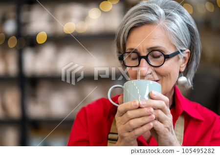 Senior craftswoman resting at pottery workshop drinking coffee. Senior craftswoman resting at pottery workshop drinking coffee. 105495282