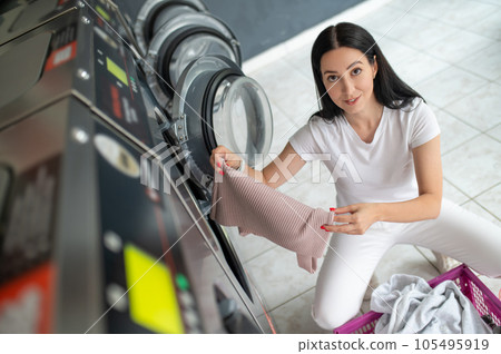 Young brunette woman sorting clothes in laundromat in the laundry. Young brunette woman sorting clothes in laundromat in the laundry. 105495919