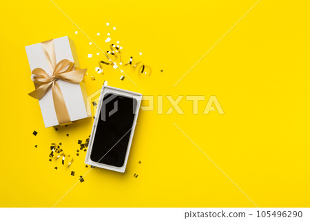 Opened gift box with gold ribbon and smartphone on color background, top view. Blank open box packaging mockup , Template for your design - branding mockup Opened gift box with gold ribbon and smartphone on color background, top view. Blank open box packaging mockup , Template for your design - branding mockup 105496290