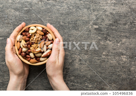 Woman hands holding a wooden bowl with mixed nuts Walnut, pistachios, almonds, hazelnuts and cashews. Healthy food and snack. Vegetarian snacks of different nuts 105496836