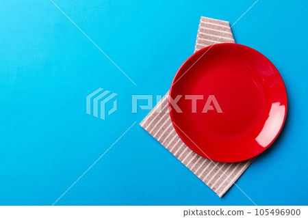Top view on colored background empty round red plate on tablecloth for food. Empty dish on napkin with space for your design 105496900