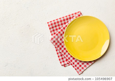 Top view on colored background empty round yellow plate on tablecloth for food. Empty dish on napkin with space for your design Top view on colored background empty round yellow plate on tablecloth for food. Empty dish on napkin with space for your design 105496907