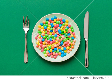 cutlery on table and sweet plate of candy. Health and obesity concept, top view on colored background cutlery on table and sweet plate of candy. Health and obesity concept, top view on colored background 105496908