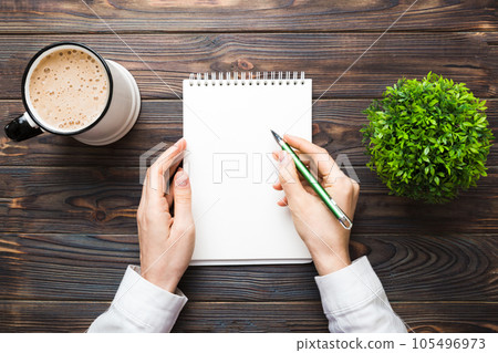 Woman hand with pencil writing on notebook and hold coffee cup. Woman working on office table with coffee 105496973