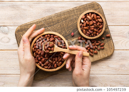 Woman hands holding a wooden bowl with peanuts. Healthy food and snack. Vegetarian snacks of different nuts Woman hands holding a wooden bowl with peanuts. Healthy food and snack. Vegetarian snacks of different nuts 105497239
