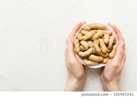 Woman hands holding a wooden bowl with close peanuts. Healthy food and snack. Vegetarian snacks of different nuts 105497242