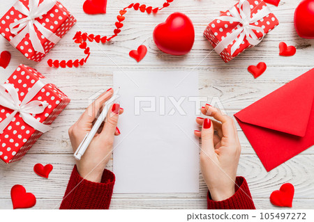 top view photo of valentine day decor female hands holding letter with envelope, small gift box and heart decoration on isolated pastel colored background with empty space top view photo of valentine day decor female hands holding letter with envelope, small gift box and heart decoration on isolated pastel colored background with empty space 105497272