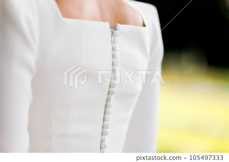 Back view of elegant white wedding dress with buttons in row down and zipper. Fashionable stylish satin dress with square neckline at back. Wedding bridal gown details. Unrecognisable person outdoors 105497333