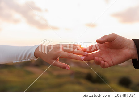 Hand of man and woman reaching and touching to each other with love on nature sunset sky background. Valentines day. Concept of human relation, community, togetherness, teamwork, love, symbolism. 105497334