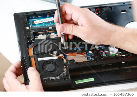 Repaiman with screwdriver fixing disassembled laptop parts. Technical support and fixing gadgets problems. Servicing, repairing, cleaning, maintaining computers. Repair shop. Hardware maintenanc 105497360