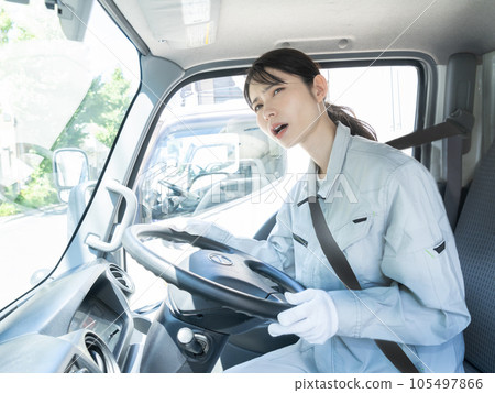A young female truck driver with a troubled face wearing work clothes sitting in the driver's seat A young female truck driver with a troubled face wearing work clothes sitting in the driver's seat 105497866