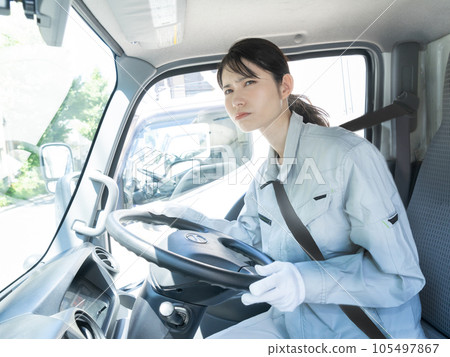 A young female truck driver with a troubled face wearing work clothes sitting in the driver's seat A young female truck driver with a troubled face wearing work clothes sitting in the driver's seat 105497867