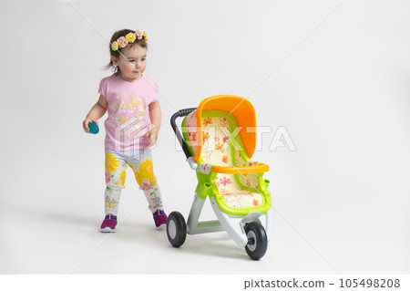 A little girl playing with a toy stroller for dolls A little girl playing with a toy stroller for dolls 105498208