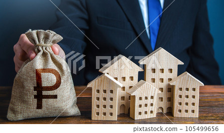 A businessman puts a russian ruble money bag near the houses. Investments in real estate assets. Municipal budget of the city. Official. Construction industry, rental business and hotel tourism. A businessman puts a russian ruble money bag near the houses. Investments in real estate assets. Municipal budget of the city. Official. Construction industry, rental business and hotel tourism. 105499656