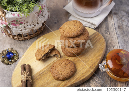 Oatmeal raisin cookies on a wooden board with cinnamon (cassia) sticks and a cup of milk. Traditional homemade pastry in rustic style. Selective focus, close-up. Oatmeal raisin cookies on a wooden board with cinnamon (cassia) sticks and a cup of milk. Traditional homemade pastry in rustic style. Selective focus, close-up. 105500147