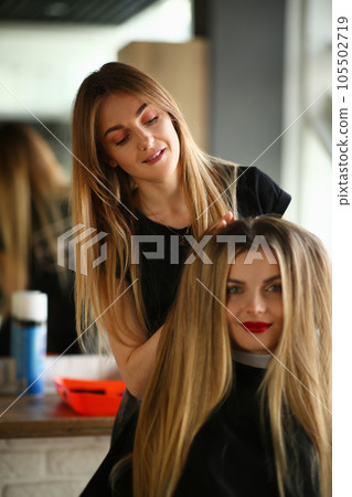 Smiling hairdresser doing hairstyle for young beautiful woman sitting in beauty salon 105502719
