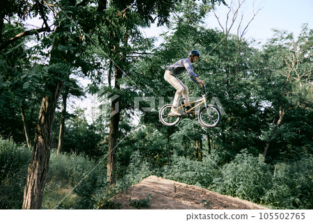 Jumping with bike. Young man, extreme sport lover riding bmx bicycle, training outdoors on hills in forest, doing tricks 105502765