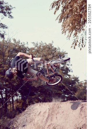 Performance. Young man in helmet training, riding bmx bike outdoors in forest. Doing dangerous looking ticks 105502784